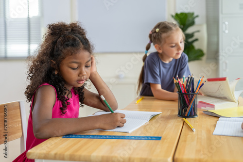 Foto African American girl writing in notebook at desk with student classmate in clas