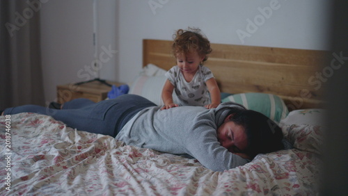 Foto Toddler climbing over resting mother on bed during lively morning play showing a