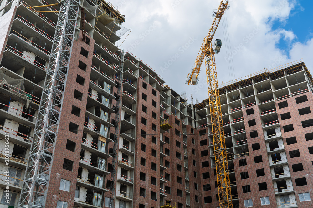 Fototapeta premium High rise residential complex grows under tower cranes with brick facade, open floors and busy urban construction site today.