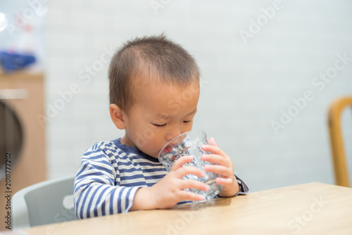 Little child sitting at wooden table and drinking water from glass