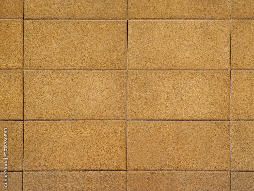 Fototapeta premium Wall of pressed concrete blocks or rectangular cobblestones with rough texture in yellowish beige or sandy yellow tone. Facade cladding surface, exterior paving, dividing and party fence background.