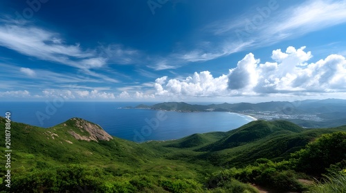 Rolling green hills frame a wide panoramic coastal view meeting the expansive blue ocean under a dramatically cloudy sky