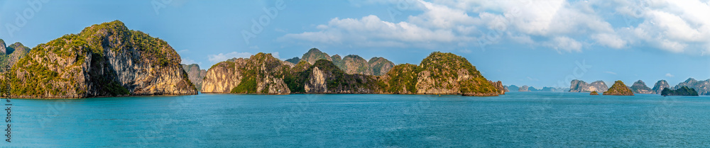 Naklejka premium A panorama view from a cruise ship passing by Karst limestone islets in Ha Long Bay, Vietnam illuminated by the evening light