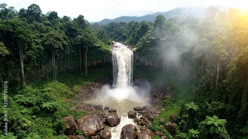 Breathtaking aerial view of a majestic waterfall cascading through lush green rainforest with sunlight