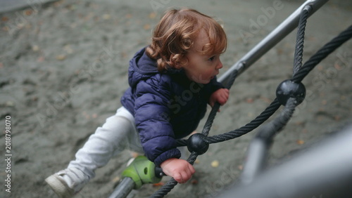 Tableau sur toile Toddler pulling on playground climbing ropes while trying to lift body upward wi