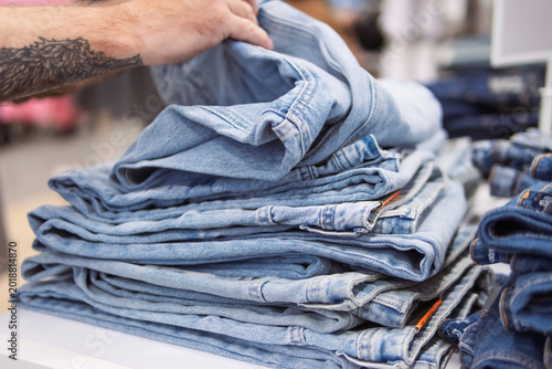 Fotografía Hand picking light blue jeans from a neatly folded stack in a clothing store, hi