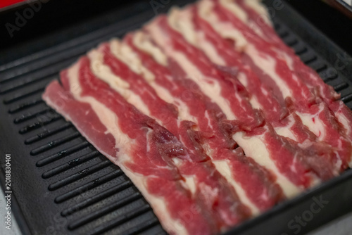 A close-up shot of sliced raw meat, arranged on a plate, ready to be cooked in a hot pot