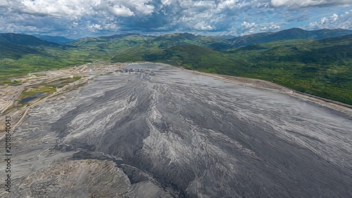 tailings. A vast, fan-shaped field of grey mine tailings contrasting with distant green hills. ESG reports, sustainability campaigns, designed for sustainability communications and ESG reporting.