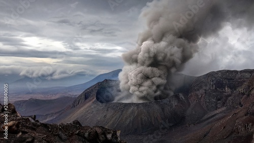 homogeneity. A thick plume of grey smoke rising from a volcanic crater, desolate landscape. ESG reports, sustainability campaigns, designed for sustainability communications and ESG reporting.