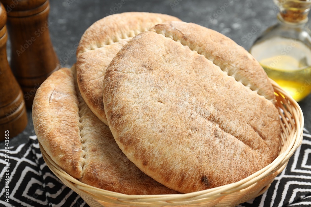 Naklejka premium Fresh pita bread in wicker basket, spices and oil on grey table, closeup
