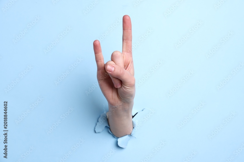 Naklejka premium Woman showing rock gesture through hole in light blue paper, closeup