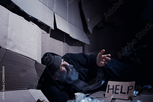 Foto A homeless bearded man sits on boxes on the street and asks for help