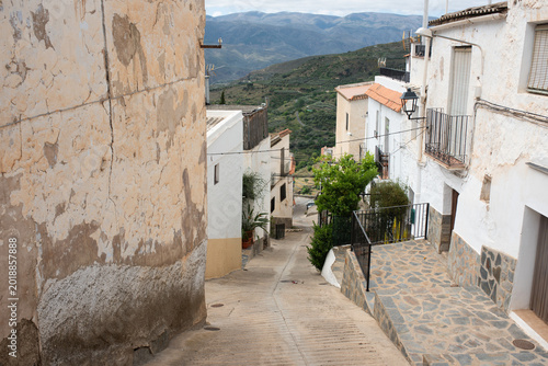 Narrow steep street in an old Spanish village with white houses and scenic mountain view.