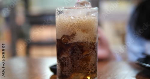 Cinematic close-up of pouring cold cola soda into a glass with ice cubes, refreshing carbonated soft drink with bubbles concept