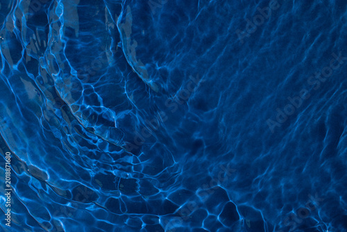 Deep dark blue shiny water with ripples, abstract texture summer form of water background. Modern dynamic toropical blue background.