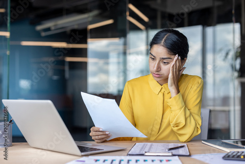 Tableau sur toile Upset and disappointed young Indian businesswoman sitting at the desk in the off