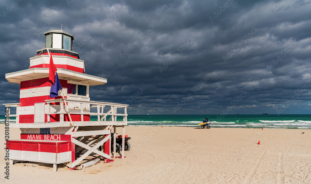 Obraz premium Lifeguard tower on the sandy Miami Beach shore. Iconic Art Deco lifeguard station under summer sky. Scenic view of South Beach coastline in Florida. Colorful lifeguard tower, symbol of Miami tourism.