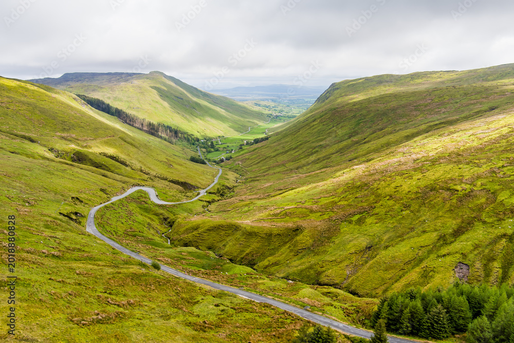 Obraz premium Aerial view of Glengesh Pass curving through a broad green valley in County Donegal, Ireland. A dramatic birds eye landscape of remote mountains and winding roads
