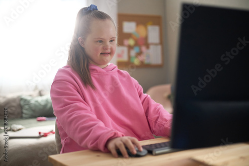 Caucasian child girl with Down syndrome using desktop computer at home, learning and navigating digital content. Supporting inclusive education, accessibility, child development campaigns