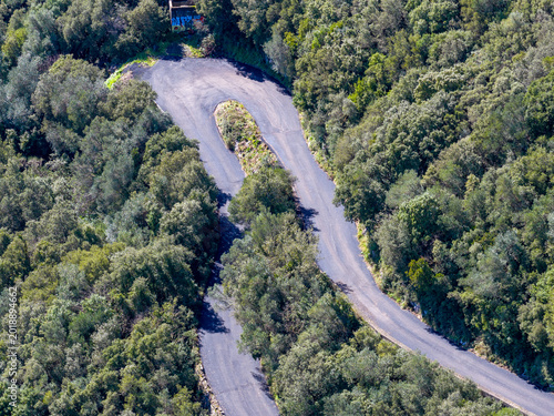 Top down view of a sharp hairpin curve on a narrow mountain pass surrounded by green trees in Sokraki, Corfu