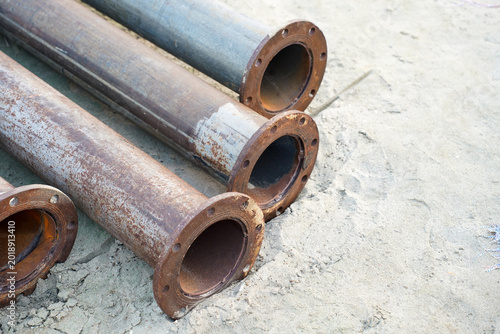 Photography Rusty metal pipes with flanges lie on sandy ground