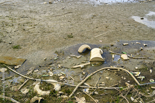 Obraz na plátne Discarded tires, metal barrel, and synthetic debris lie in river mud on exposed Danube bank