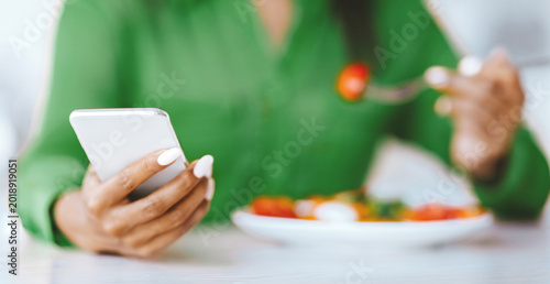 Schilderij op canvas A person is using a smartphone in one hand while holding a fork with salad in the other