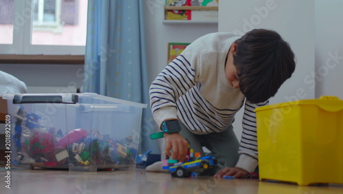 Tableau sur toile Child playing with toy vehicle on floor near storage bins, focused imagination a