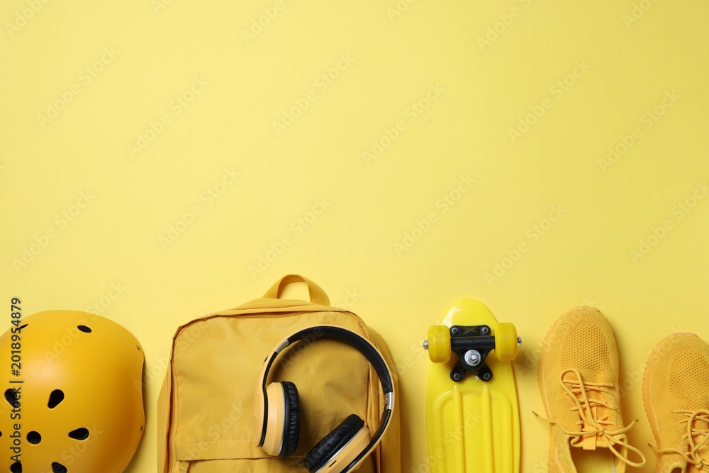 Fototapeta premium Sports equipment. Backpack, headphones, penny board, helmet and sneakers on yellow background, flat lay. Space for text