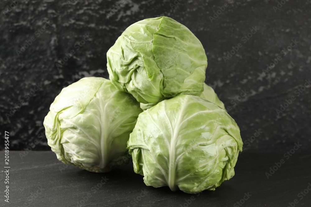Fototapeta premium Fresh cabbages on black textured table, closeup