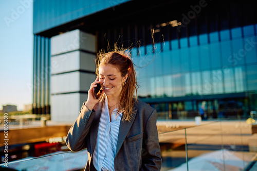 Foto Young businesswoman smiling while communicating on her mobile phone, managing bu