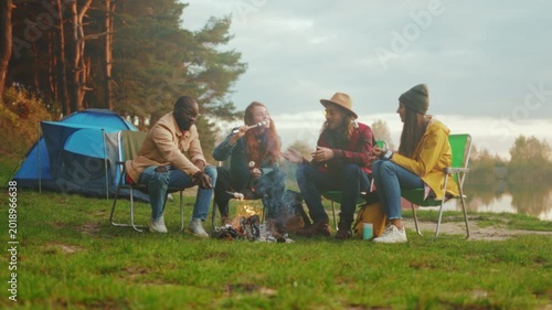 Friends sharing stories, Evening camping adventure sharing tales and enjoying warmth beside peaceful lakeside