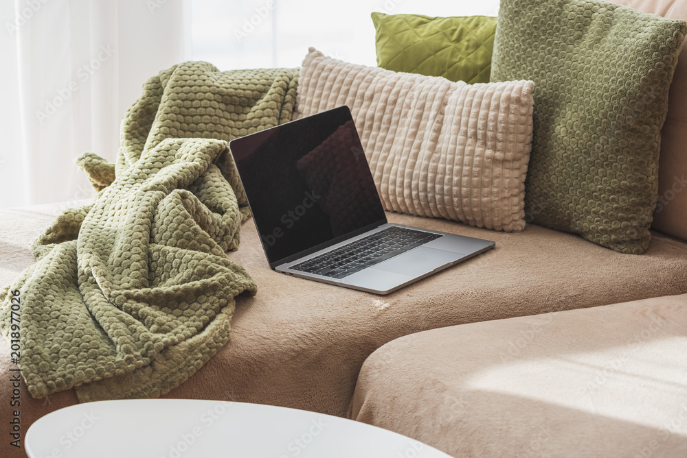 Fototapeta premium Laptop on Cozy Sofa with Textured Pillows and Blanket. Relaxed Home Workspace
