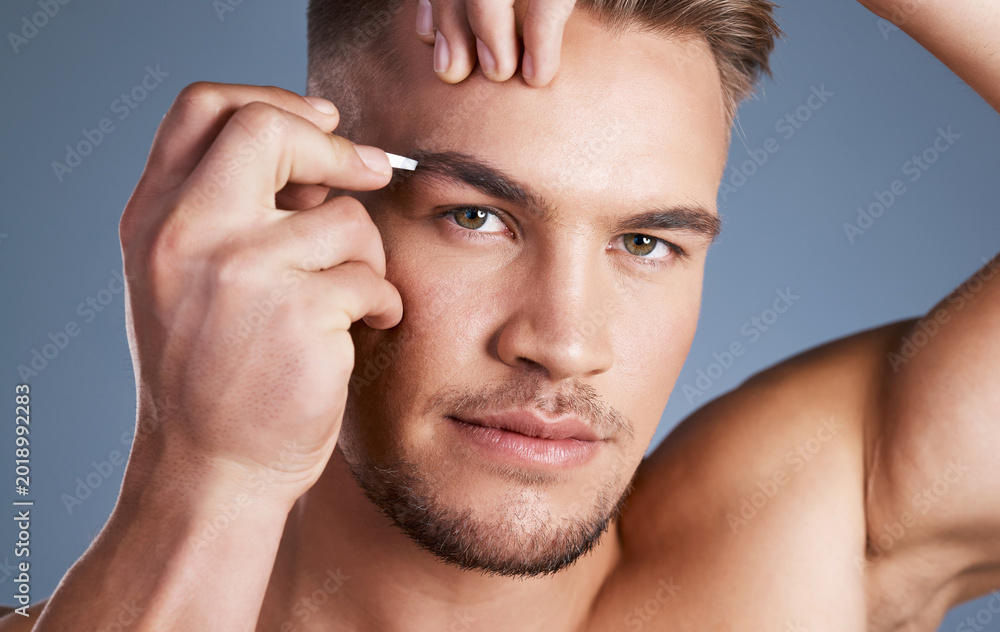 Fototapeta premium Grooming, tweezing or man in studio with portrait, hair removal or facial care in cosmetics. Wellness, serious or person with beauty tool, polished appearance or brow maintenance on gray background.