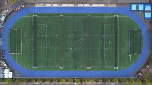 Flight above soccer stadium with blue running track encircling the artificial turf football field in a North America city
