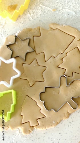 Vertical video: Pressing metal plastic cutters into rolled cookie dough on speckled counter to bake