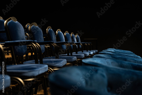 Dimly Lit Cushioned Chairs Near Stage, Closeup Perspective Reveals Upholstery Texture And Worn Comfort, Hush Of Rehearsal And Intimate Cinematic Mood