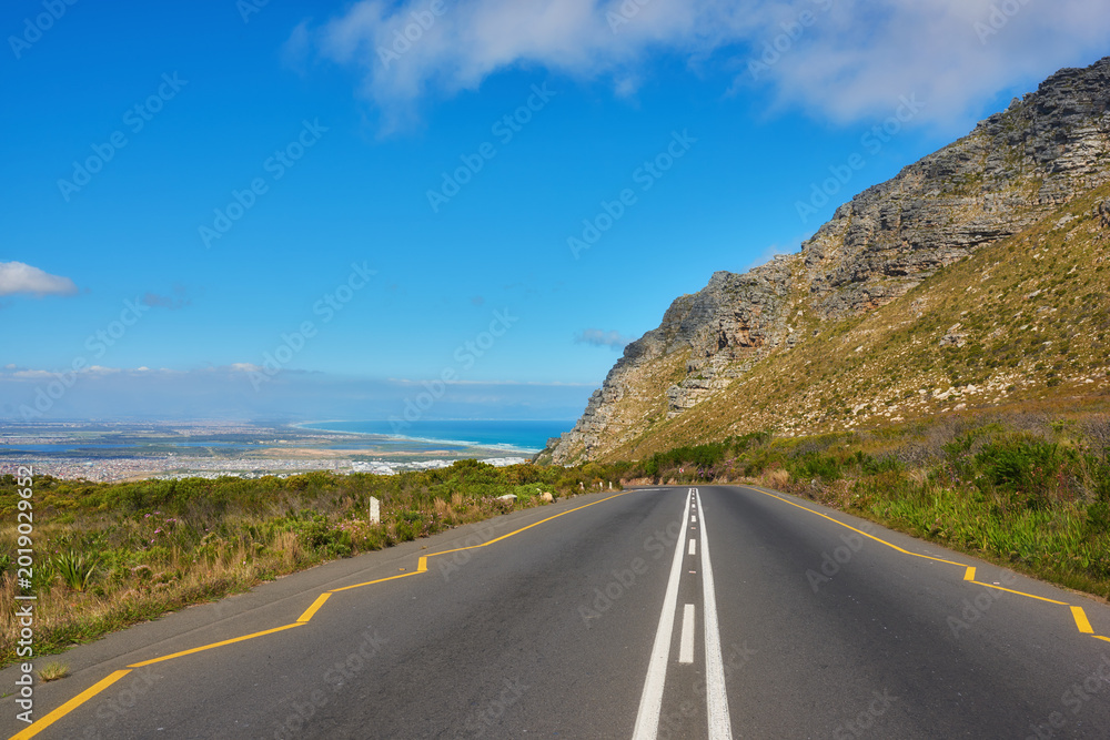 Obraz premium Landscape, blue sky and road on mountain for travel, tourist destination or journey to ocean. Empty, background and street with scenic route, highway and nature for vacation, trip or holiday by coast