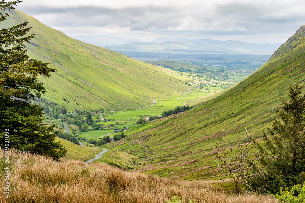 Naklejka premium Glengesh Pass winding through a green mountain valley in County Donegal, Ireland. A scenic road landscape of the Wild Atlantic Way and remote Irish highlands.