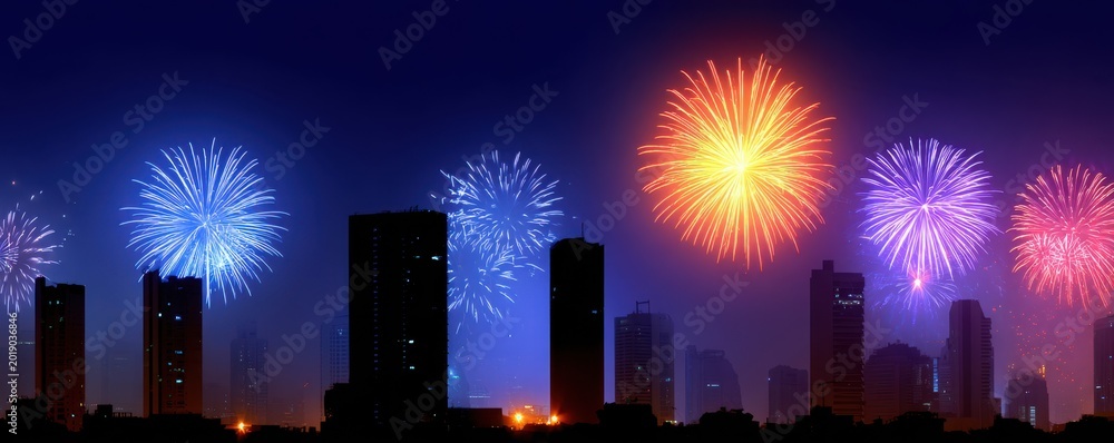 Obraz premium Colorful fireworks display over a city skyline at night, illuminating buildings with vibrant bursts of light in various colors