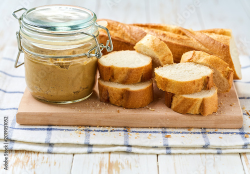 slices French baguette bread scattered on a table and jar with natural gourmet liver pate .