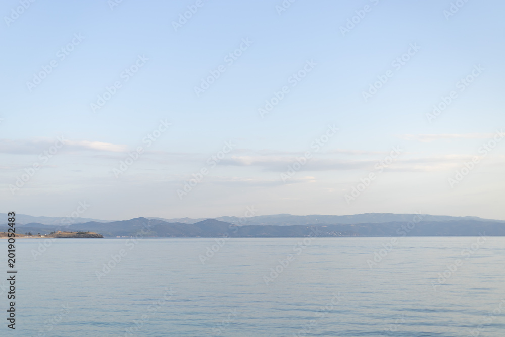 Fototapeta premium Calm Serene Seascape with Distant Mountains and Clear Blue Sky