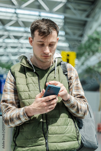 Foto Young male traveler using smartphone while standing in modern airport departure