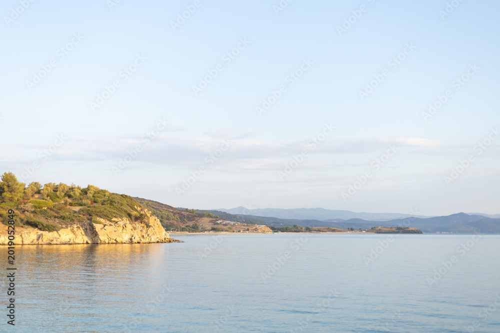 Fototapeta premium Golden hour light on calm Mediterranean sea and rocky coast with hills