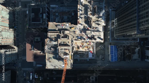 Top down showing crane building new skyscraper in downtown area, surrounded by tall office buildings with shadows and moving traffic on city streets below