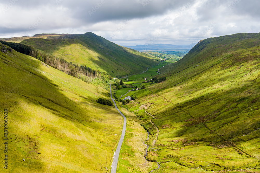 Obraz premium Aerial view of Glengesh Pass curving through a broad green valley in County Donegal, Ireland. A dramatic birds eye landscape of remote mountains and winding roads
