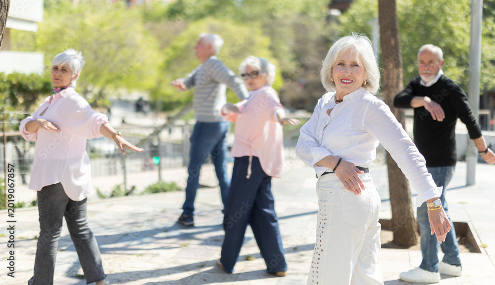 Fototapeta premium Active senior people doing arm swing exercise while practicing healthy lifestyle in open-air