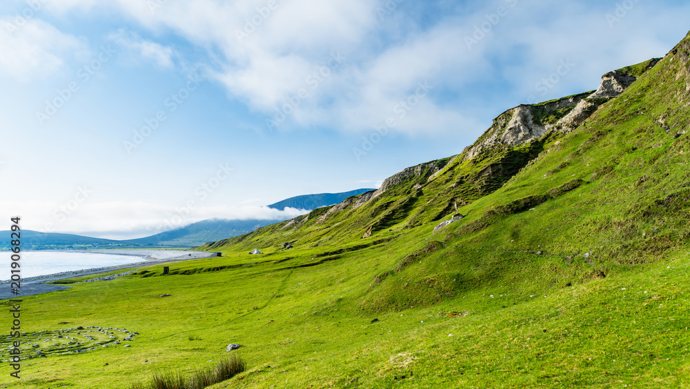 Naklejka premium Southern Keel Beach on Achill Island, County Mayo, Ireland, with green coastal slopes above the shore. This image shows the quieter grassy edge of the beach.