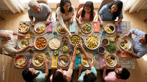 Top view of a large smiling multi-generation Indian family sharing a traditional meal around a rustic wooden table