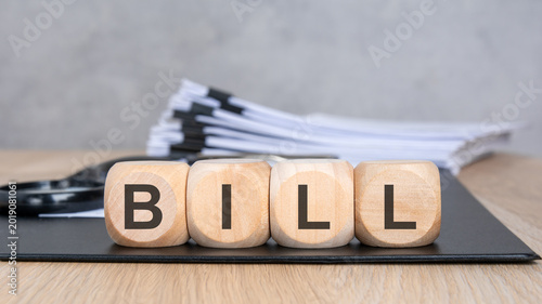 Wooden blocks with BILL text, blurred documents and magnifying glass.